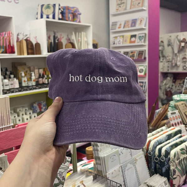 Purple cap with 'hot dog mom' text held in a store setting