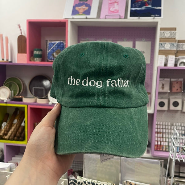 Green cap with 'the dog father' text held in front of a store shelf.